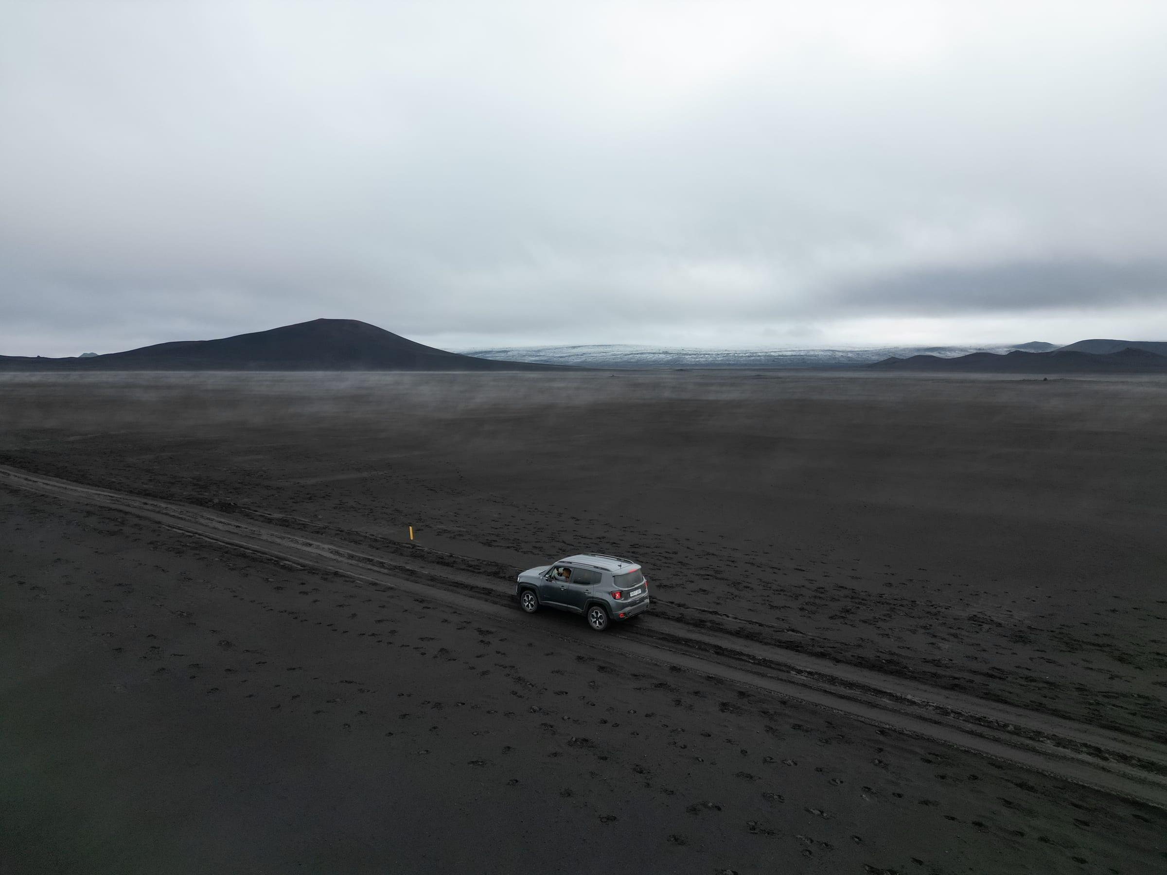 4x4 following a track across a black volcanic sand plain in the Icelandic highlands, glacier on the horizon